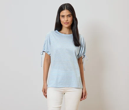 Une femme portant un t-shirt à rayures bleues et blanches à manches courtes et un pantalon beige sur un fond clair.
