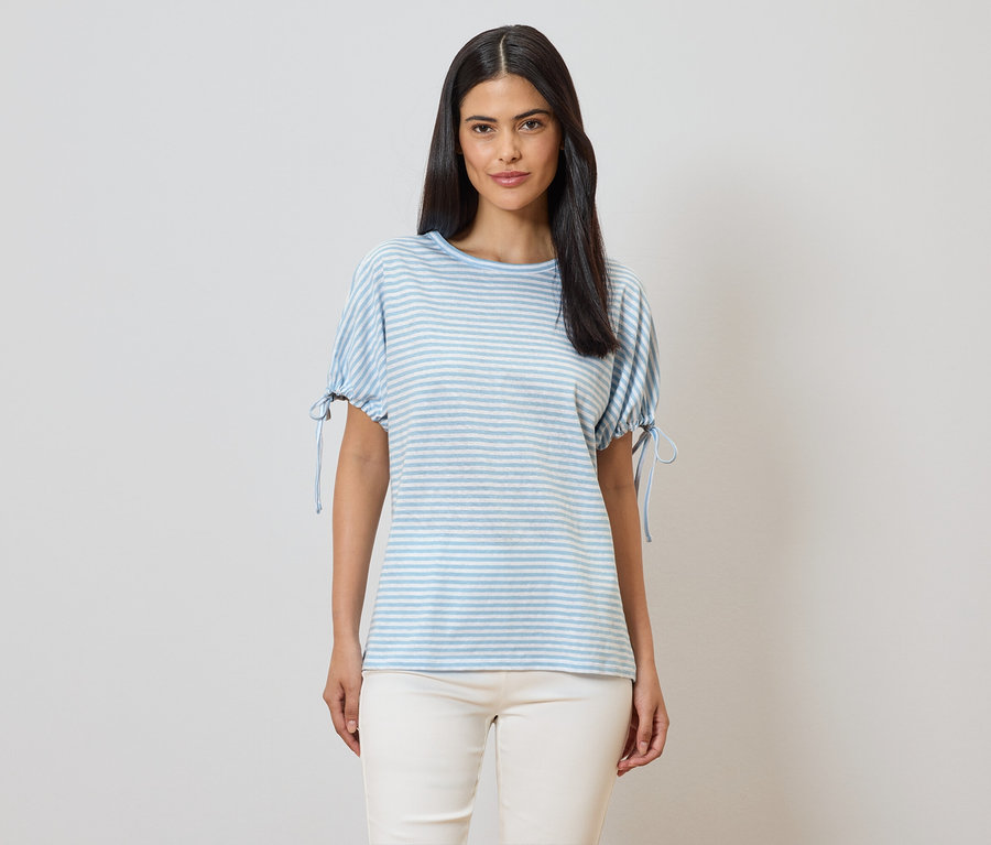 Une femme portant un t-shirt à rayures bleues et blanches à manches courtes et un pantalon beige sur un fond clair.