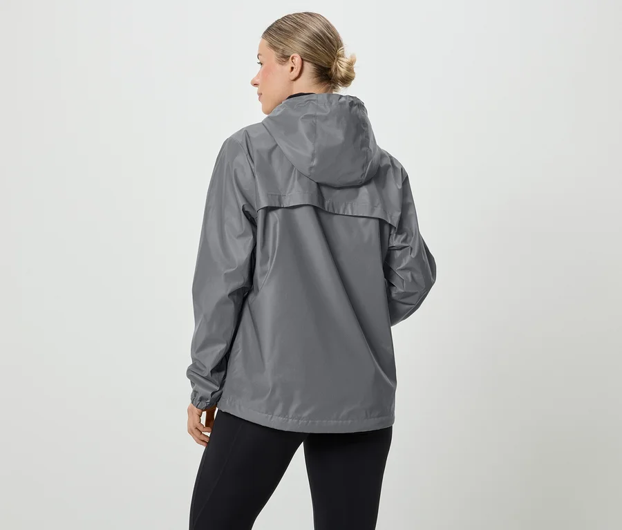 Une femme aux cheveux blonds porte un imperméable gris à capuche et un legging noir, vue de dos.