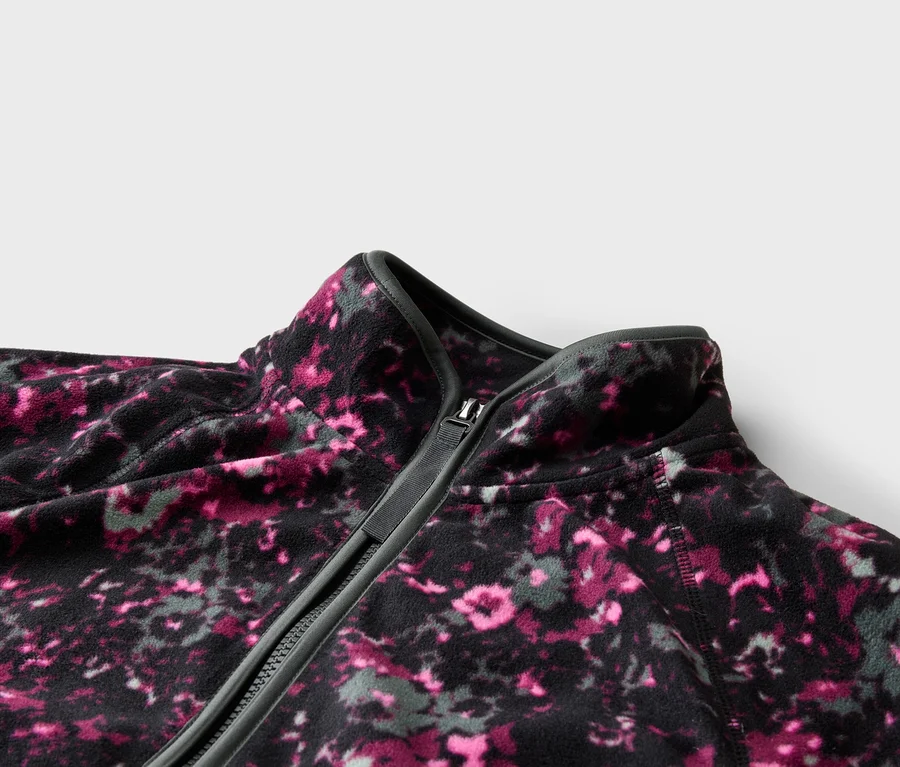 Gros plan d'une veste en polaire zippée avec un motif floral abstrait rose et gris.