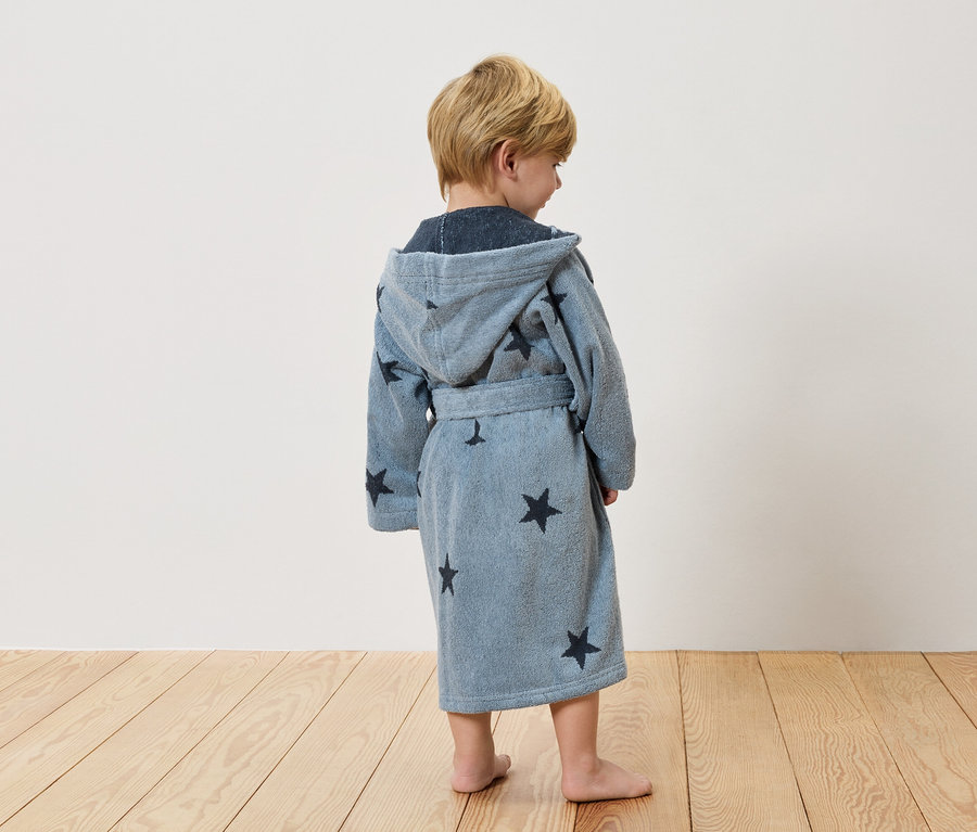 Un enfant, vu de dos, porte un peignoir bleu clair à étoiles.