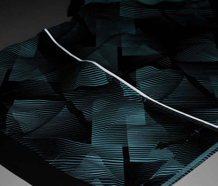 Gros plan d'un vêtement avec un motif géométrique répétitif en noir et turquoise, accentué par une bande blanche.