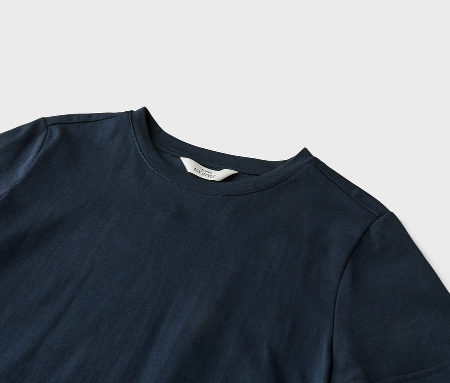 Gros plan d'un t-shirt bleu marine avec une étiquette blanche indiquant « ICHIBO MY STYLE » au niveau du col, posé sur un fond gris clair.