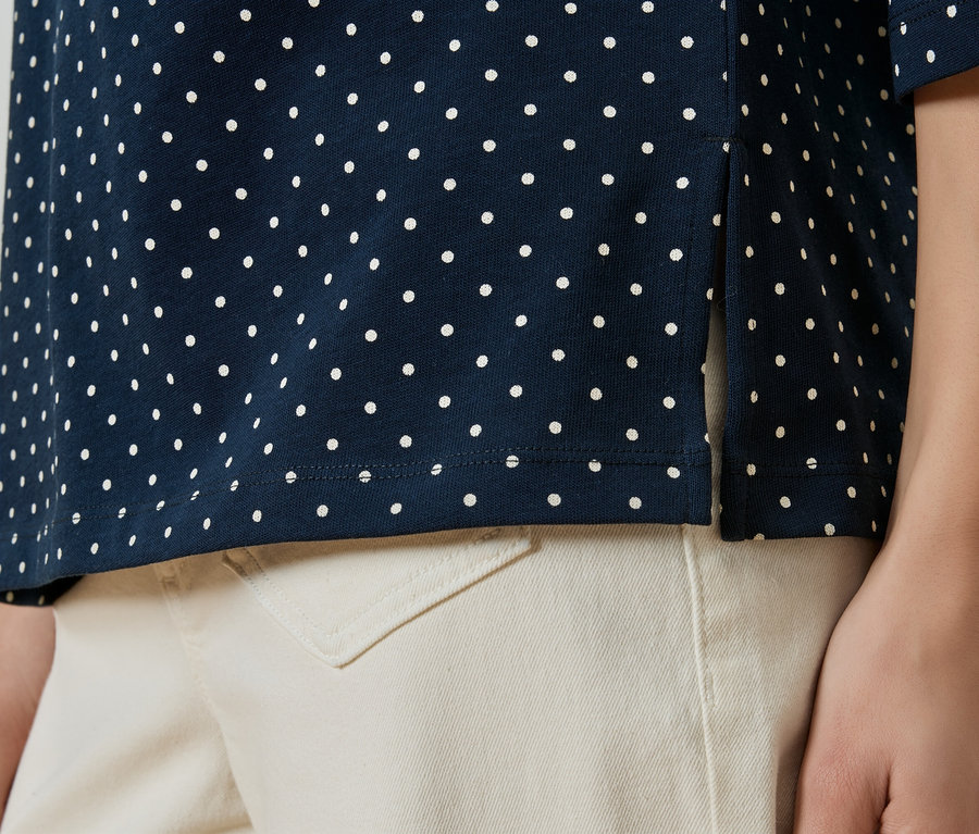 Gros plan d'une personne portant un polo bleu marine à pois et un pantalon beige.