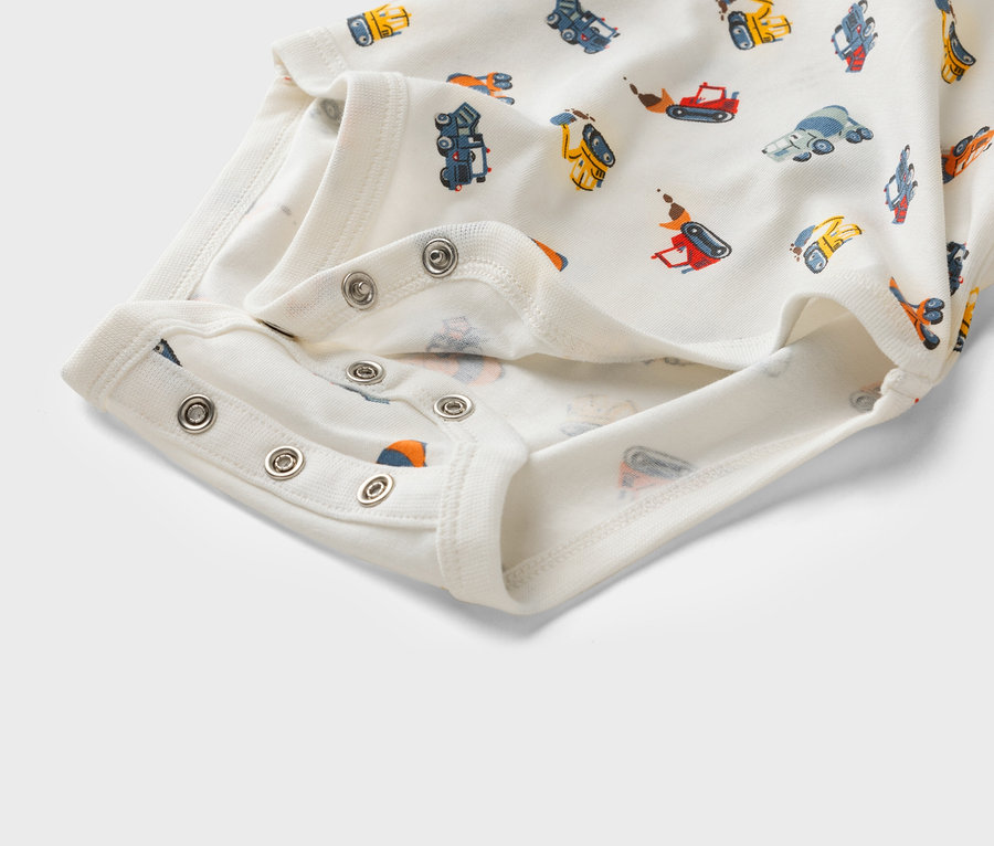 Gros plan sur un body blanc pour bébé avec un motif de véhicules de chantier et des boutons-pression.