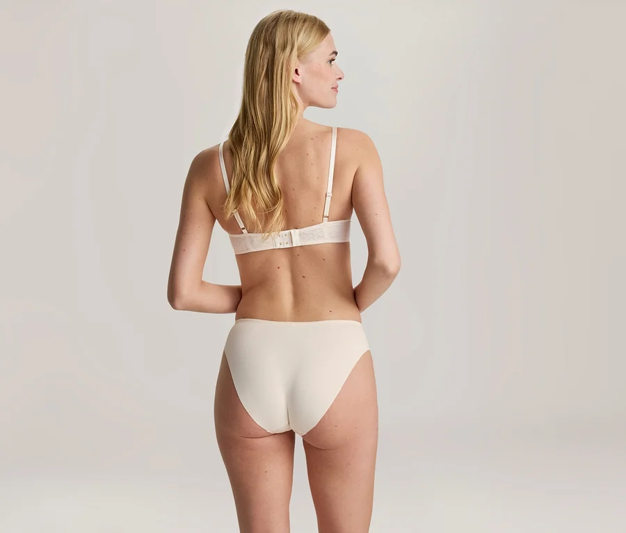 Femme blonde vue de dos, portant un soutien-gorge et une culotte de couleur claire, regardant vers la droite.