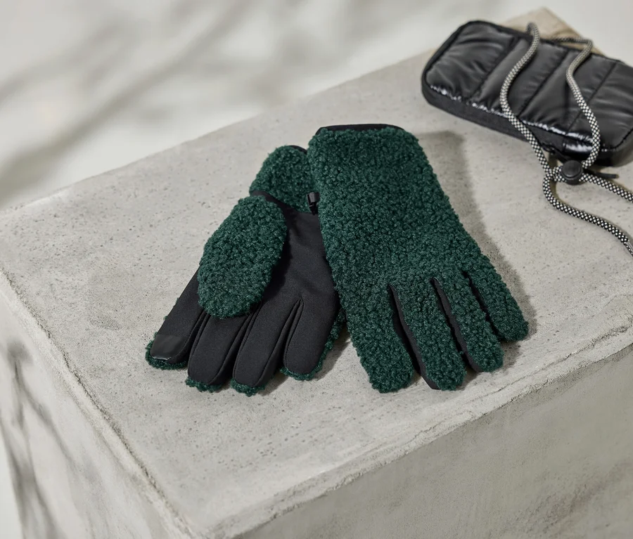 Une paire de gants verts texturés avec des paumes noires repose sur un bloc de béton à côté d'une pochette matelassée noire avec un cordon de serrage moucheté.