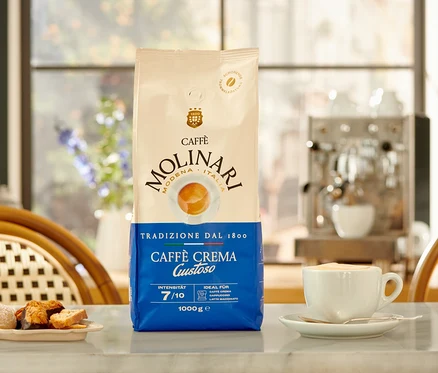 Un paquet de Caffè Molinari Caffè Crema Gustoso, une tasse de café et une assiette de biscuits sur une table.