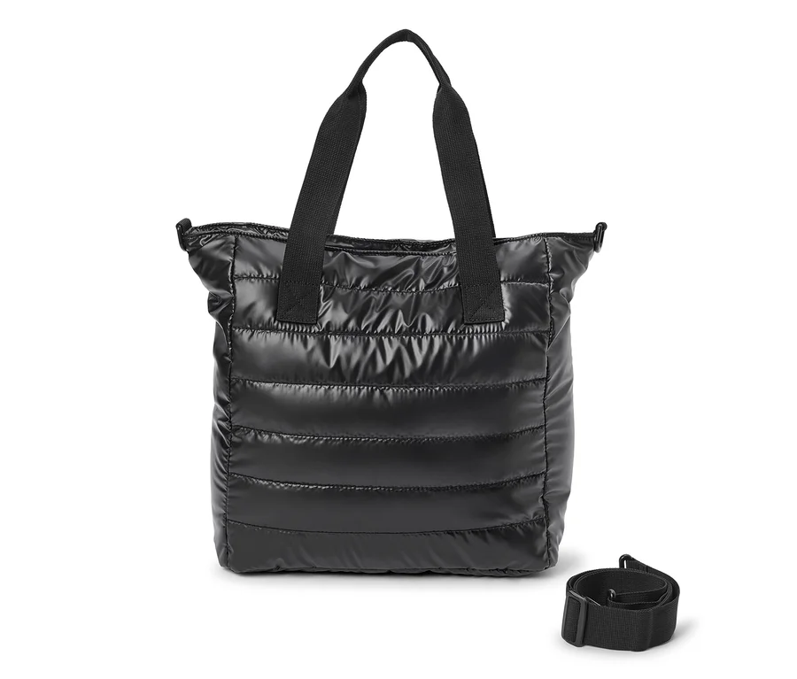Sac cabas matelassé noir avec deux poignées et une fermeture éclair, une bandoulière noire détachée est posée à côté.