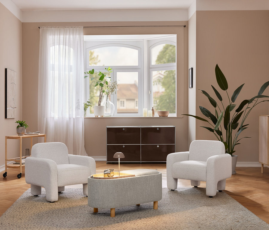 Un salon confortable avec deux fauteuils gris clair et un pouf assorti sur un tapis. Une lampe de table à LED sans fil beige est posée sur une armoire en bois clair à côté d'une grande plante. Un meuble de rangement marron foncé se trouve sous une fenêtre en baie.