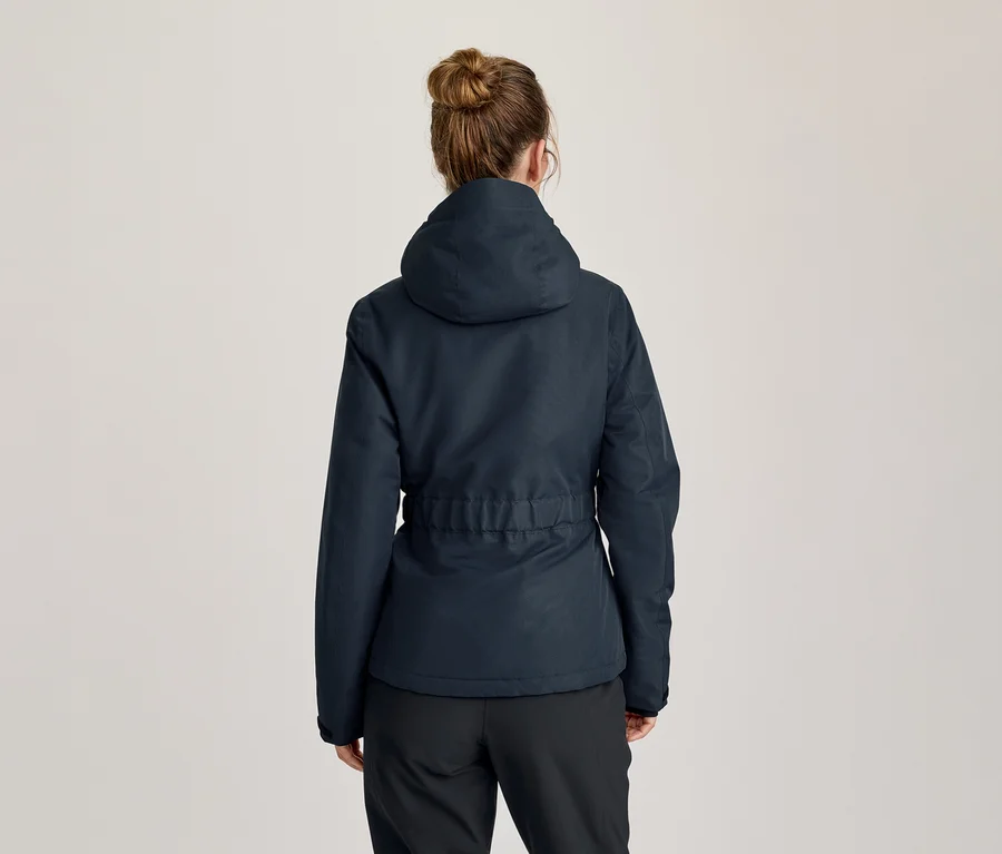 Femme vue de dos, portant une veste à capuche bleu foncé avec une taille ajustable et un pantalon noir. Ses cheveux sont attachés en chignon.