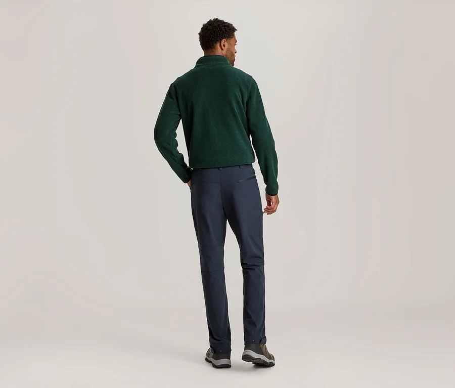 Homme vu de dos, portant un pull en polaire vert foncé et un pantalon bleu marine. Sa main droite est dans sa poche.