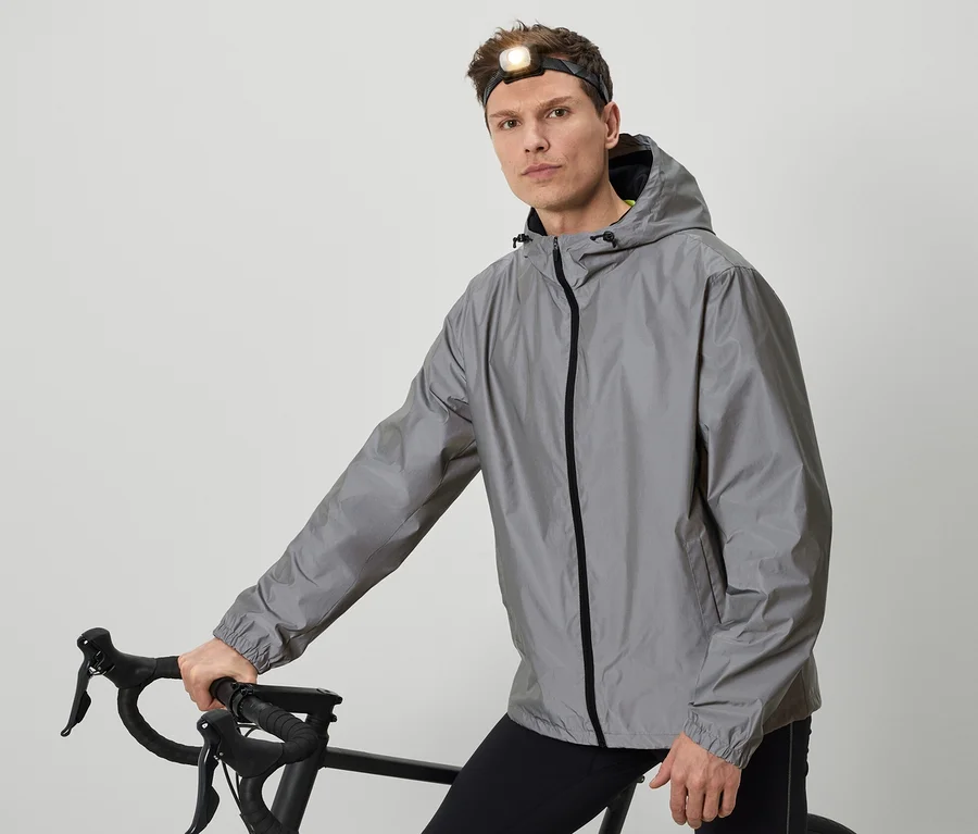 Un homme avec une lampe frontale pose avec un vélo vêtu d'une veste grise.