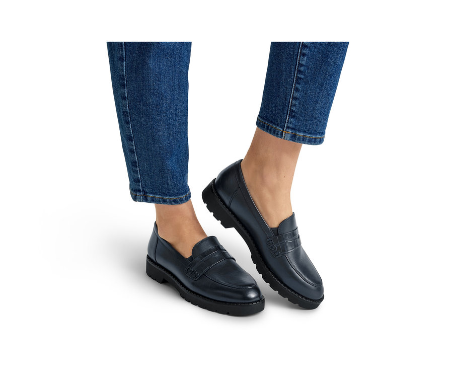 Jambes et pieds d'une personne portant un jean bleu et des mocassins bleu foncé à semelles épaisses noires.