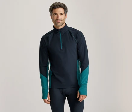 Homme debout, portant un haut à manches longues bleu foncé avec un quart de zip et des accents turquoise sur les côtés et les avant-bras, et un pantalon de couche de base bleu foncé.