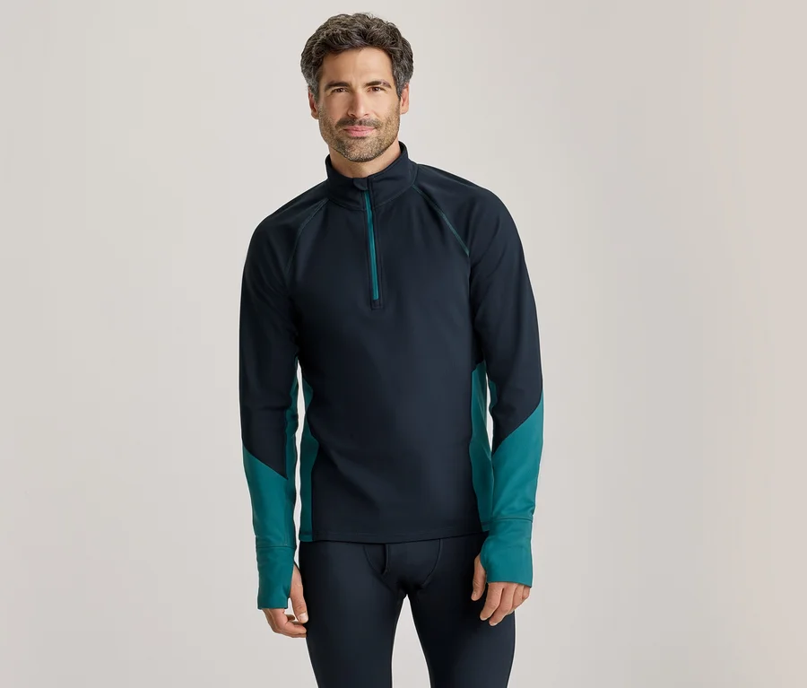 Homme debout, portant un haut à manches longues bleu foncé avec un quart de zip et des accents turquoise sur les côtés et les avant-bras, et un pantalon de couche de base bleu foncé.