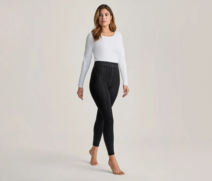 Femme portant un haut blanc à manches longues et des leggings noirs à motif pied-de-poule, debout pieds nus.