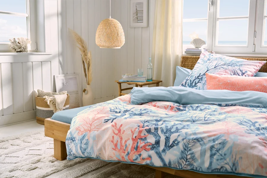 Chambre avec un lit, un drap-housse en microfibre bleu clair pour lit double, une parure de lit en renforcé et deux taies d'oreiller en microfibre bleu clair et deux corail. Une suspension est suspendue au-dessus du lit.