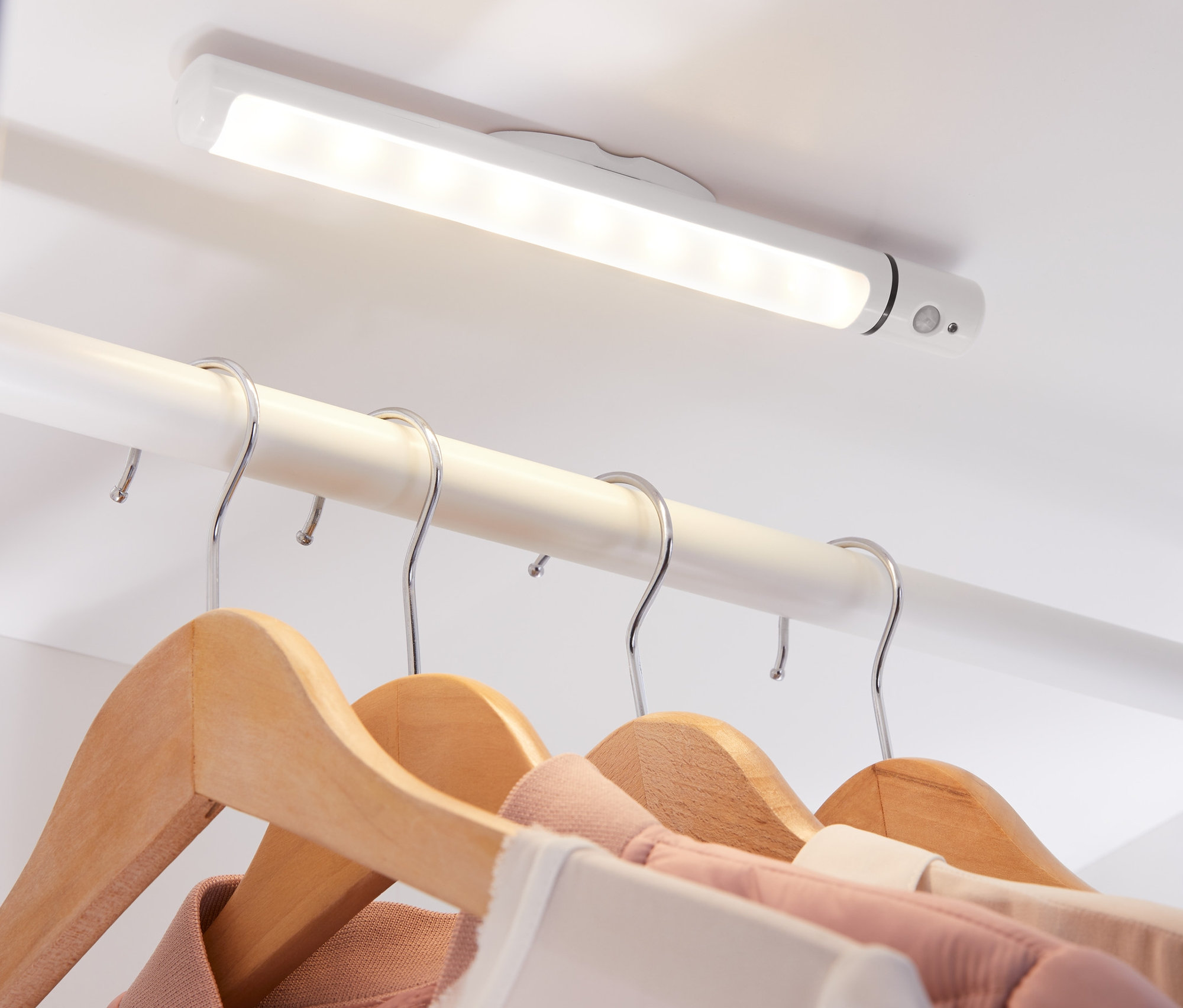 Une lampe multifonction à LED fixée au plafond d'un placard illumine des vêtements suspendus à des cintres en bois.