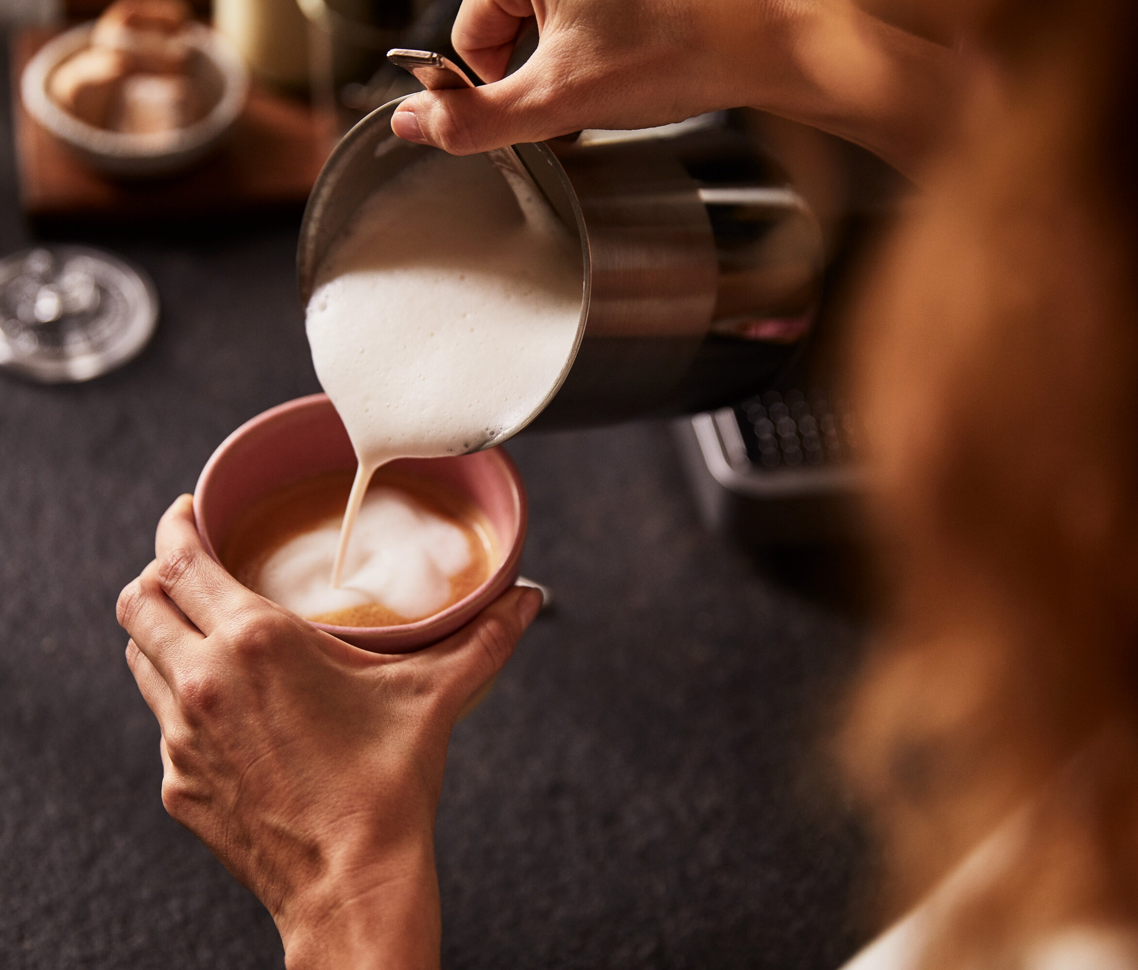 Une femme verse du lait mousseux d'un mousseur à lait manuel dans une tasse de café rose.