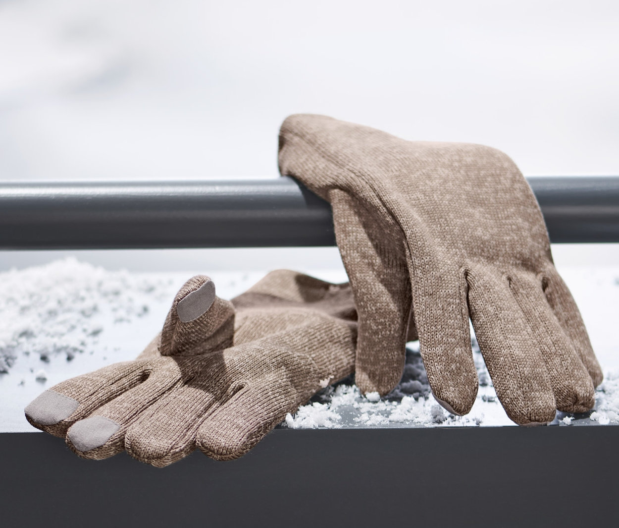 Des gants marron en matière polaire tricotée sont posés sur une surface enneigée.