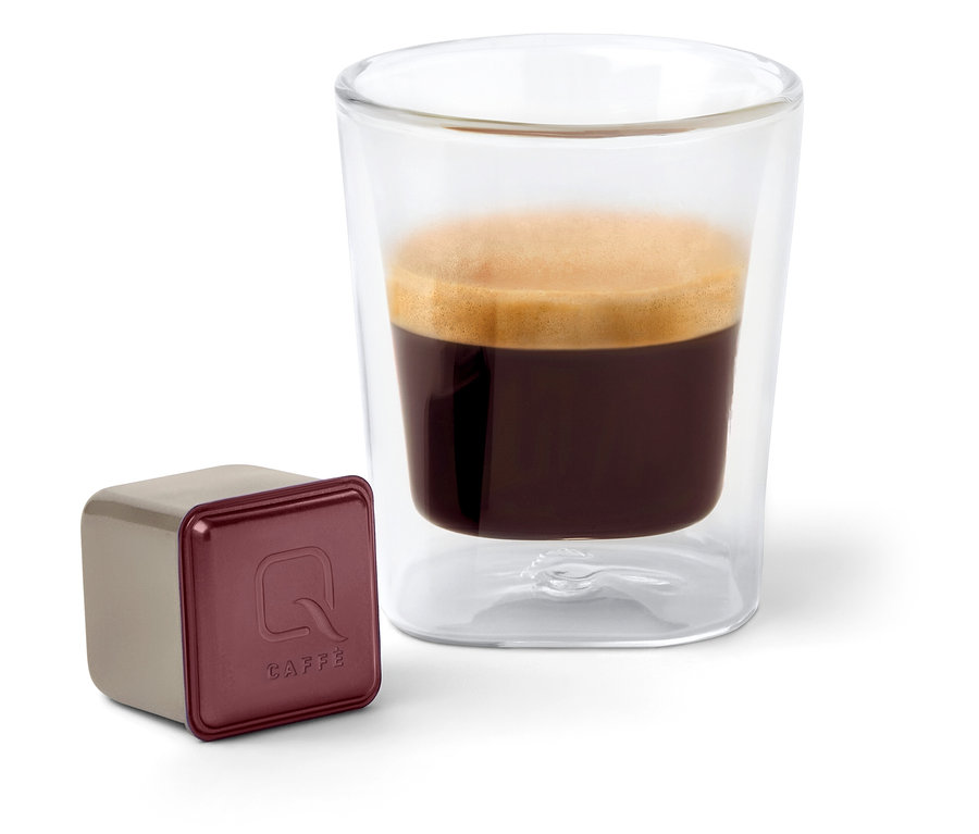 Une capsule Qbo Caffè KINYAA GALERAS est posée à côté d'un verre de café.