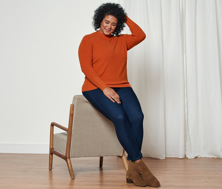 Une femme assise sur une chaise porte un pull en maille, un jegging et des bottines en cuir velours.
