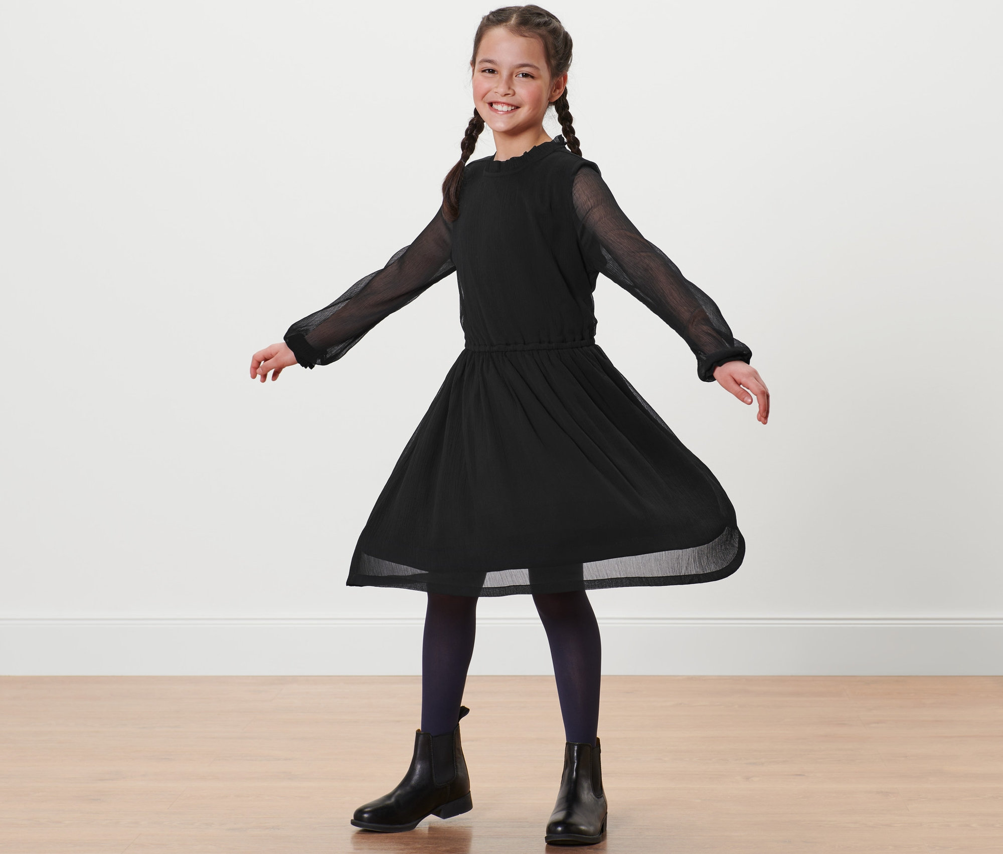 Fillette souriante avec des tresses debout en robe noire en chiffon.