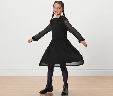 Fillette souriante avec des tresses debout en robe noire en chiffon.