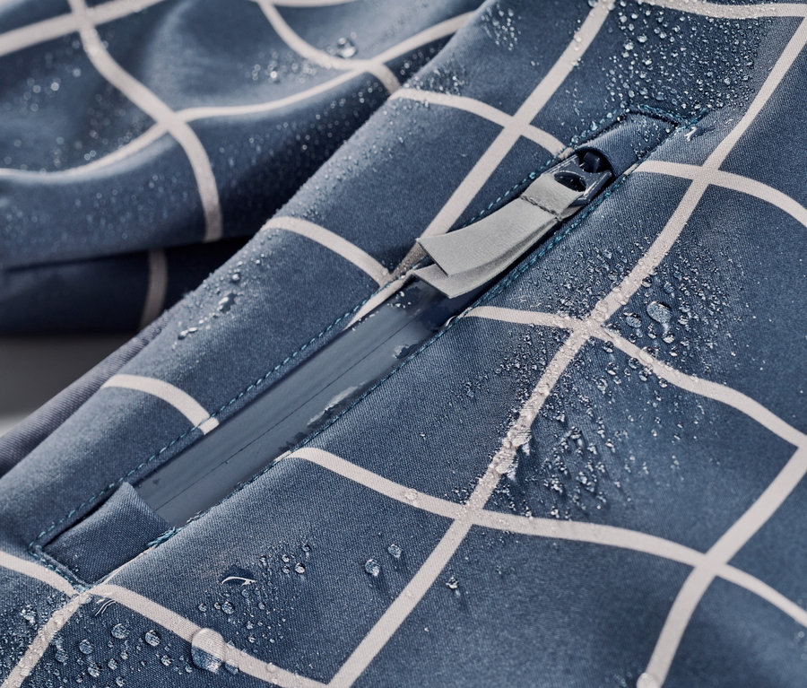 Gros plan sur une combinaison softshell à carreaux pour enfant avec fermeture éclair et gouttes d'eau.