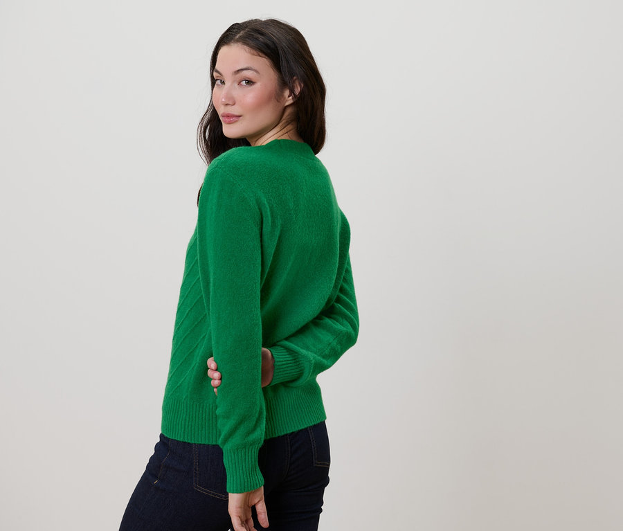 Femme regardant par-dessus son épaule portant un cardigan vert avec une structure tricotée.