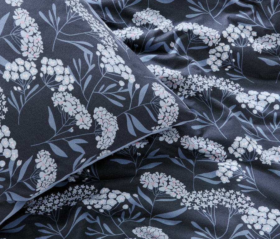 Gros plan d'une parure de lit en jersey d'hiver bleu marine avec des fleurs blanches et des feuilles bleues.
