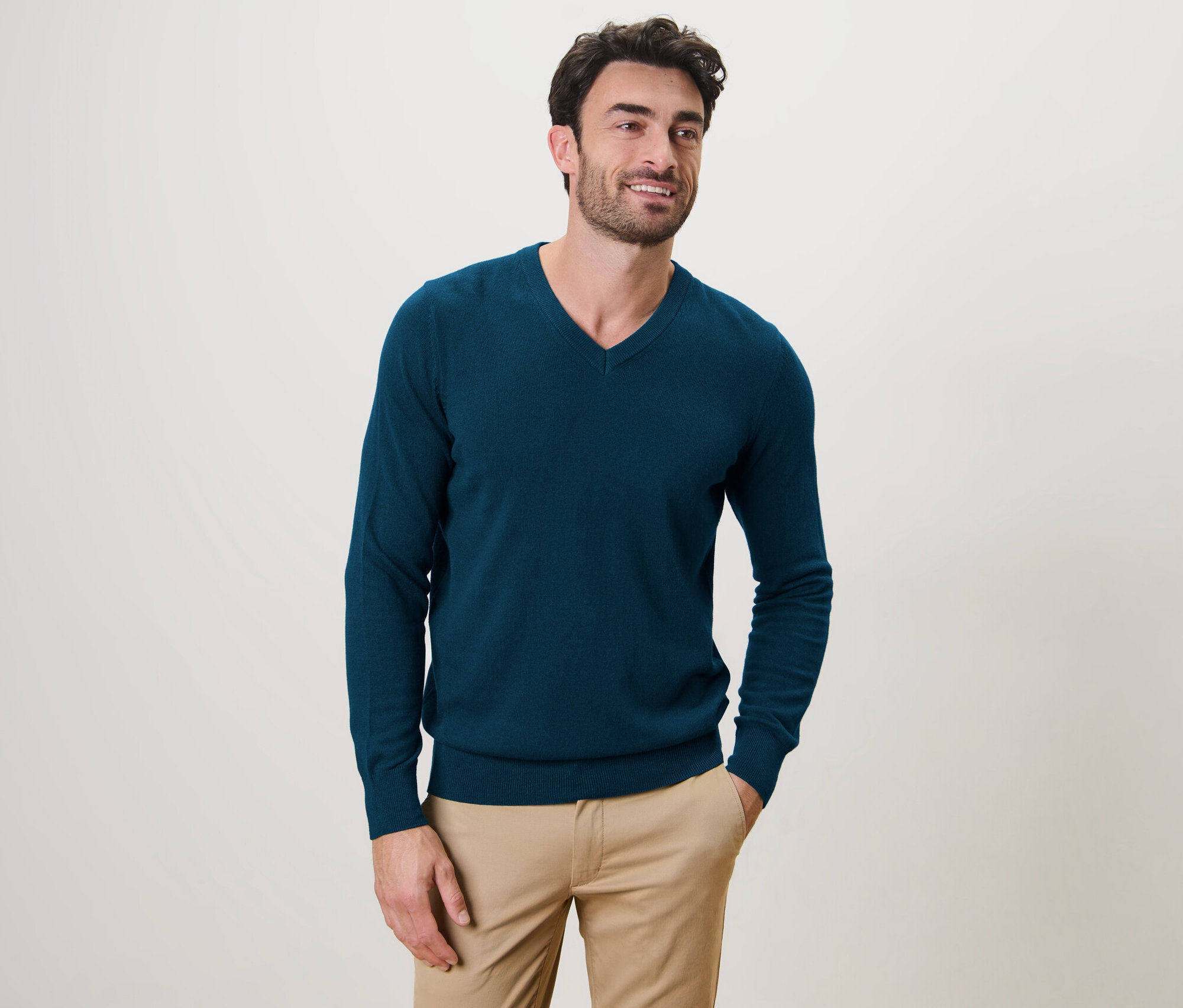 Un homme pose et porte un pull pétrole à encolure en V.