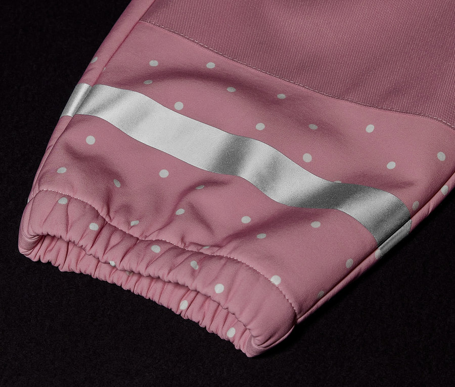 Détail d'une combinaison en softshell pour enfant avec une manche rose, des points blancs et une bande réfléchissante.