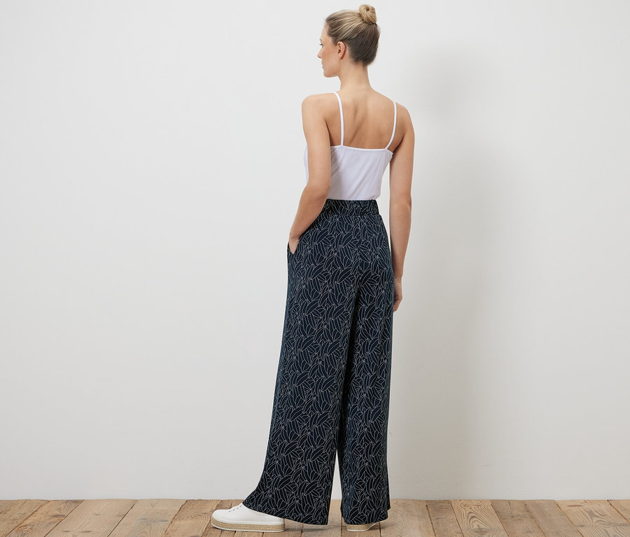 Une femme, vue de dos, porte un pantalon palazzo imprimé bleu foncé et blanc crème.