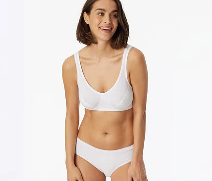 Femme souriante portant un soutien-gorge blanc et un hipster SCHIESSER blanc, les mains sur les cuisses.