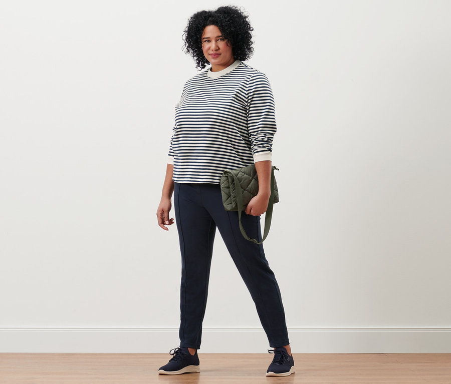Femme posant avec un sac matelassé à bandoulière, un pantalon de jogging avec nervure et un sweat-shirt à rayures.