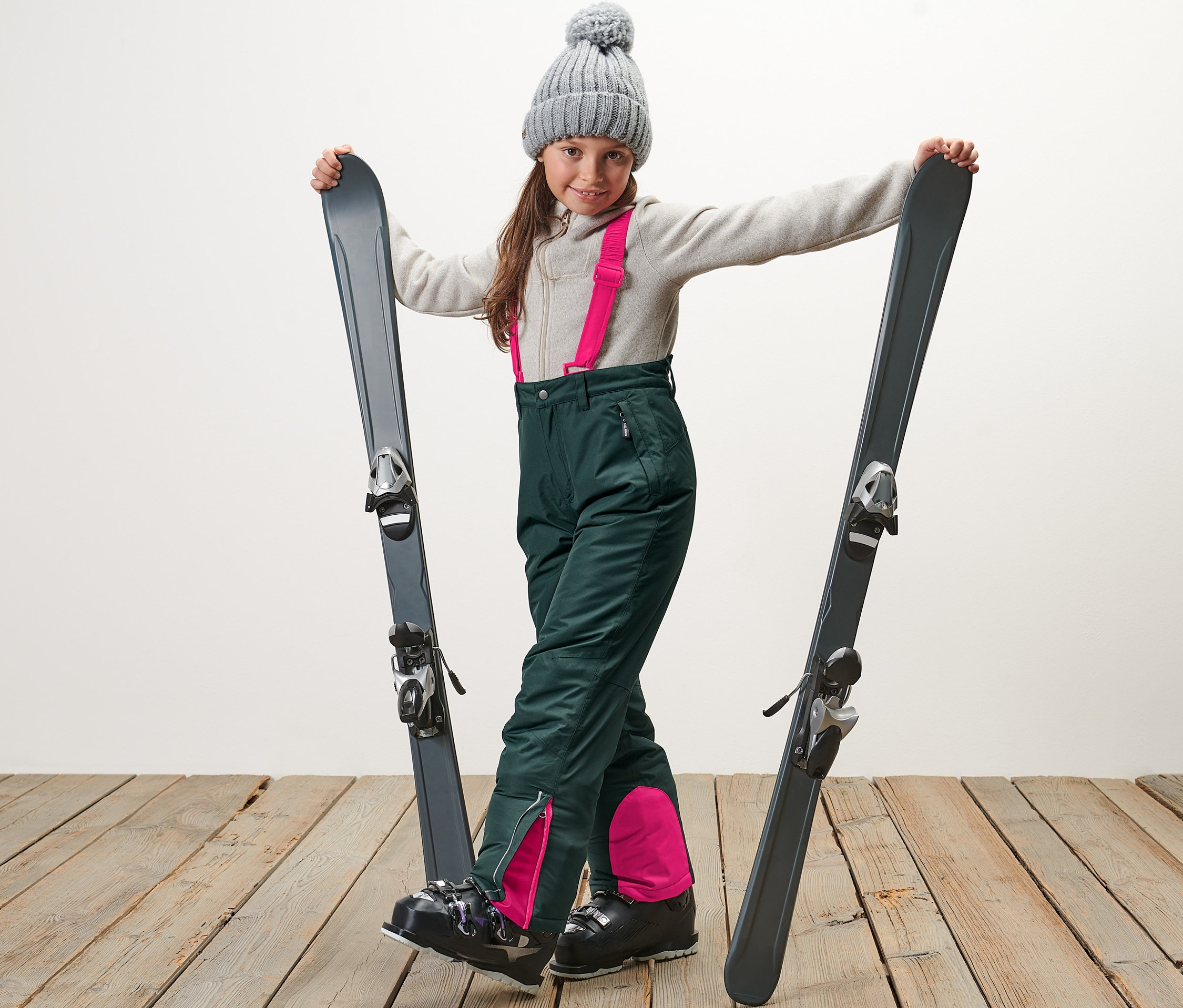 Fille debout avec des skis en pantalon de ski pour enfant vert foncé.