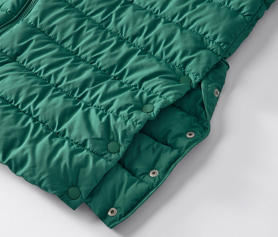 Gros plan sur un manteau matelassé à capuche vert avec des boutons-pression.