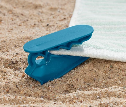 Une pince à linge bleue maintient une serviette sur le sable. 4 pinces à linge.