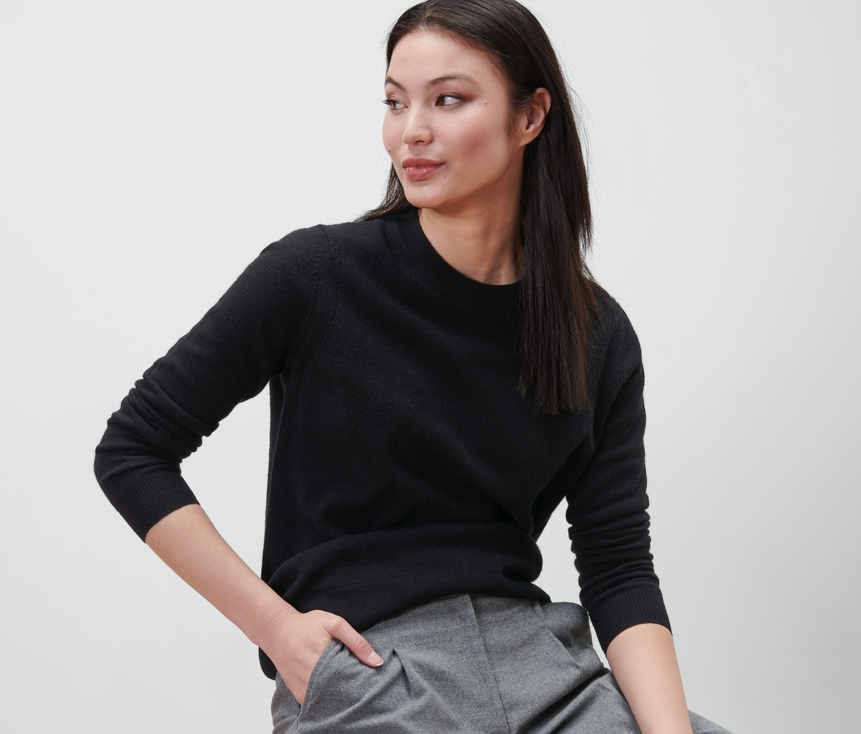 Une femme est assise sur un tabouret et porte un pull noir en maille fine avec du cachemire.