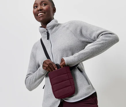 Une femme en polaire grise met un smartphone dans une pochette isolante.