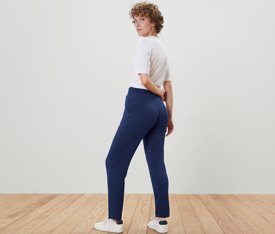 Une femme regarde par-dessus son épaule et pose en pantalon en jersey bleu foncé.