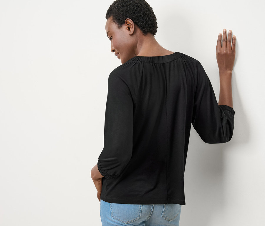 Femme vue de dos portant une blouse avec fronces et un jean.