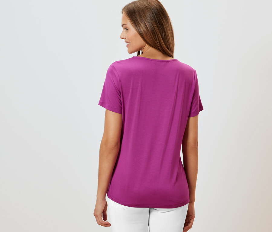 Femme vue de dos portant un t-shirt avec soufflet, baie et un pantalon blanc.