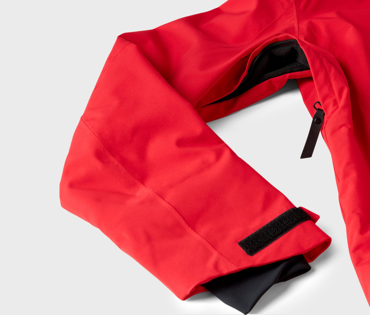 Détail d'une veste rouge avec poche zippée et manchette Velcro.
