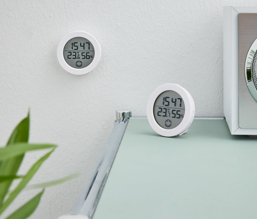 Deux horloges numériques blanches. Une horloge est sur le mur. La deuxième horloge est posée sur une table à côté d'une radio blanche.