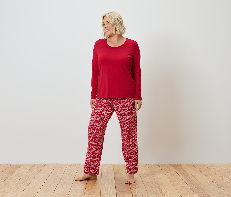 Une femme blonde se tient sur un plancher en bois et porte un pyjama rouge.