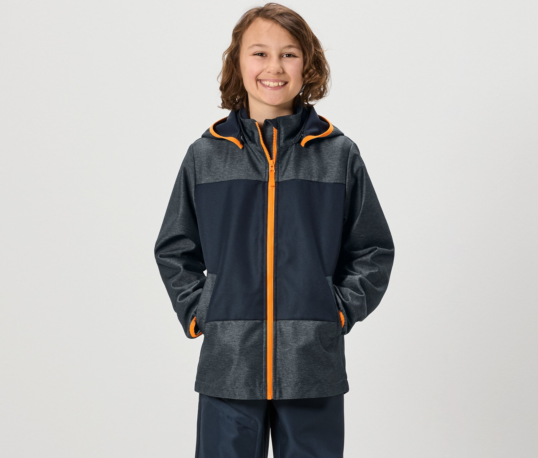 Garçon souriant portant une veste softshell Kinder avec les mains dans les poches.