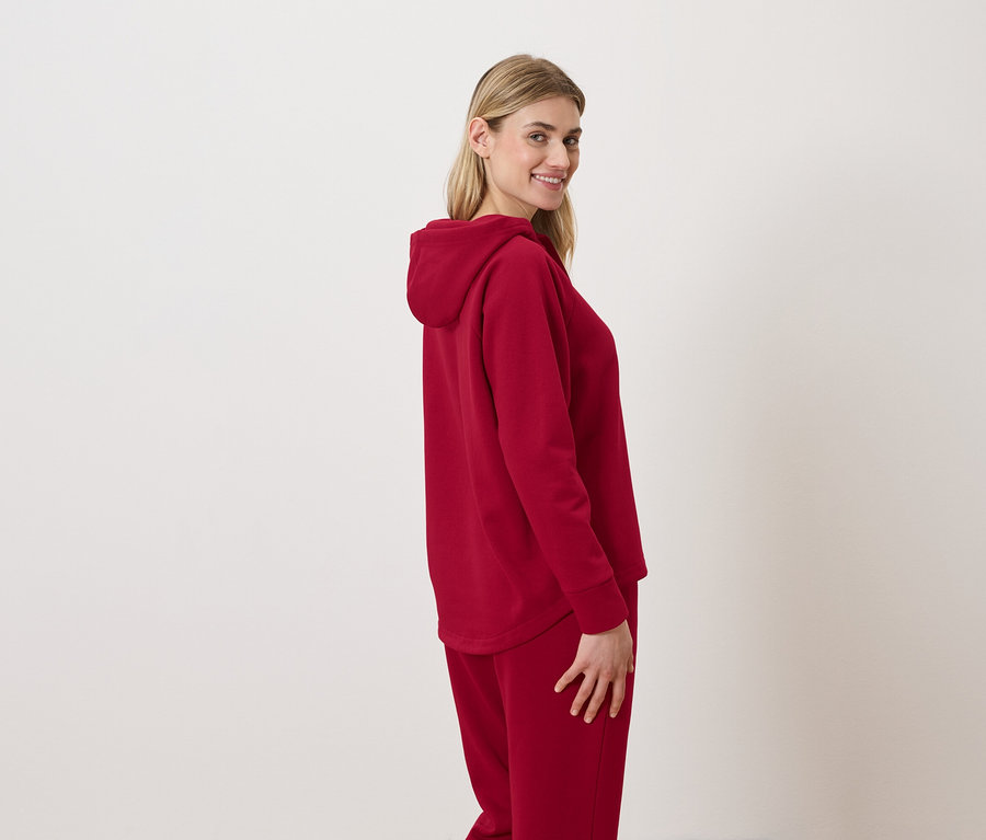Femme en survêtement à capuche rouge souriant par-dessus son épaule.